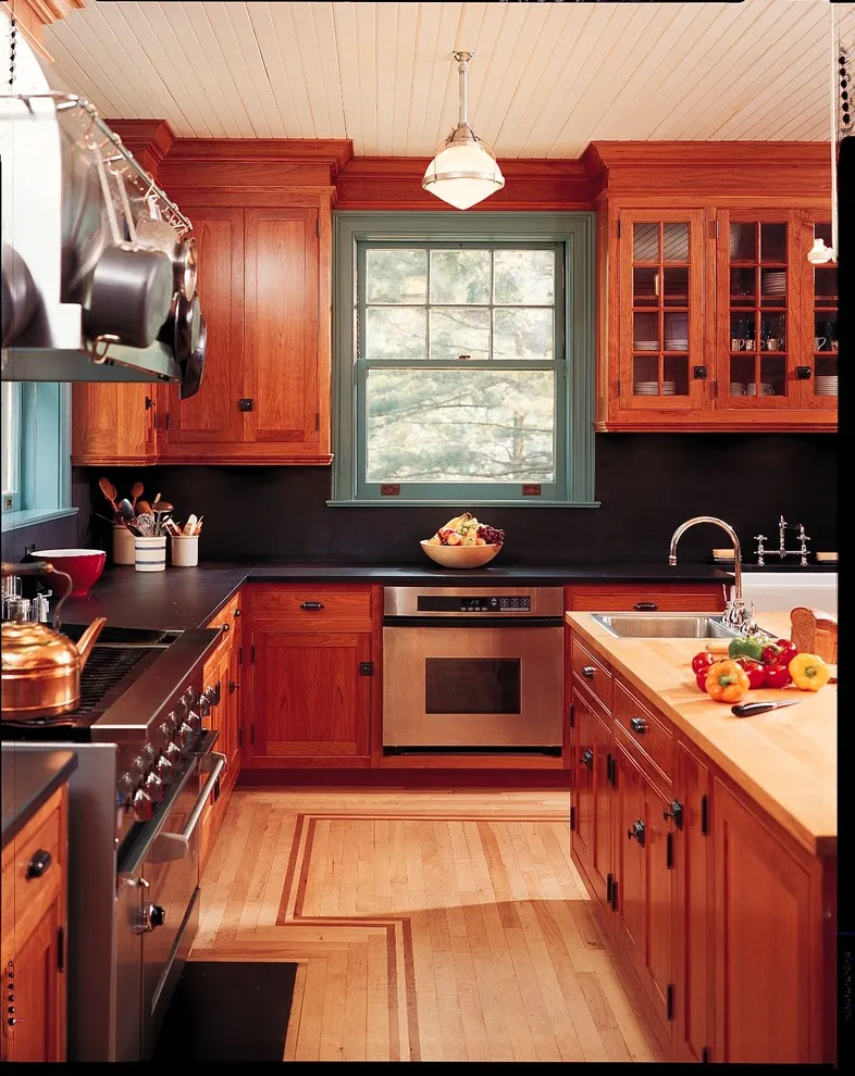Reddish wood cabinets surround a small kitchen with a dark backsplash and bright window