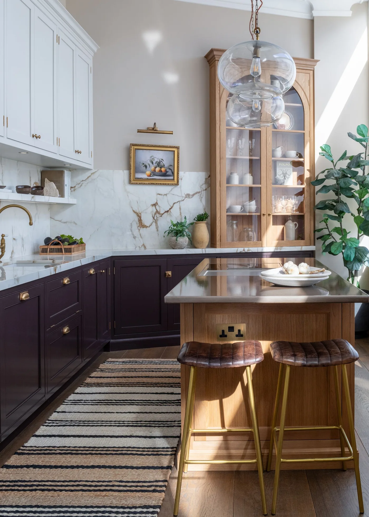 Deep brown lower cabinets beside a lighter wood island, white uppers and a tall glazed dresser.