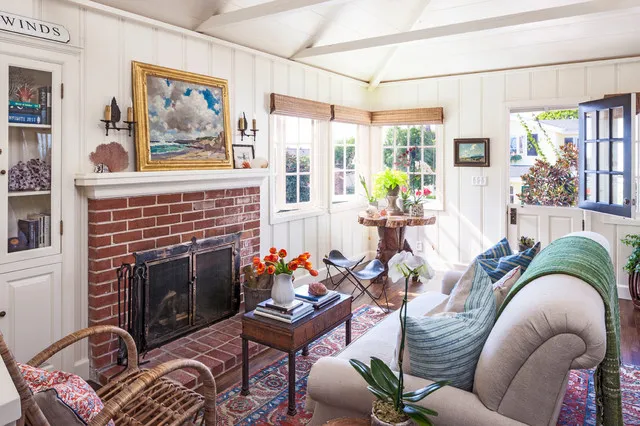 Pale seating sits around a red brick fireplace with framed art nearby.