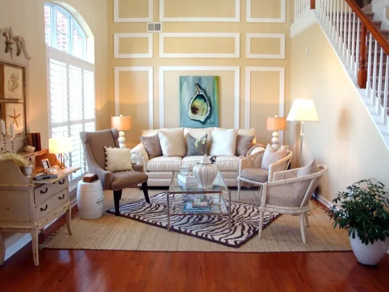 Tall pale sitting room with a shell picture, light sofa and chairs, and a zebra-patterned rug over a larger tan rug.