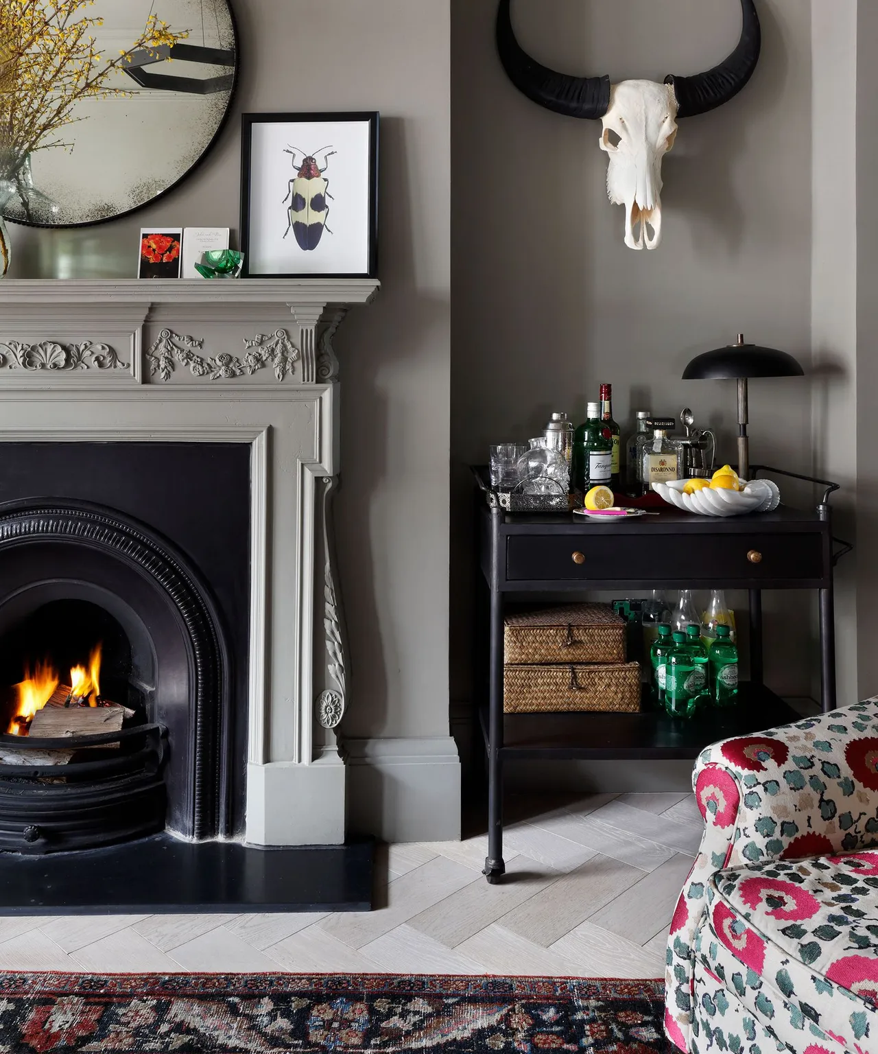 Dark gray walls frame a decorative fireplace beside framed pictures and a small cabinet.