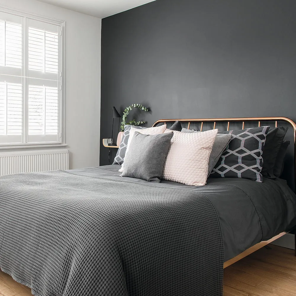 A dark gray wall stands behind a deep bedspread beside bright white shutters