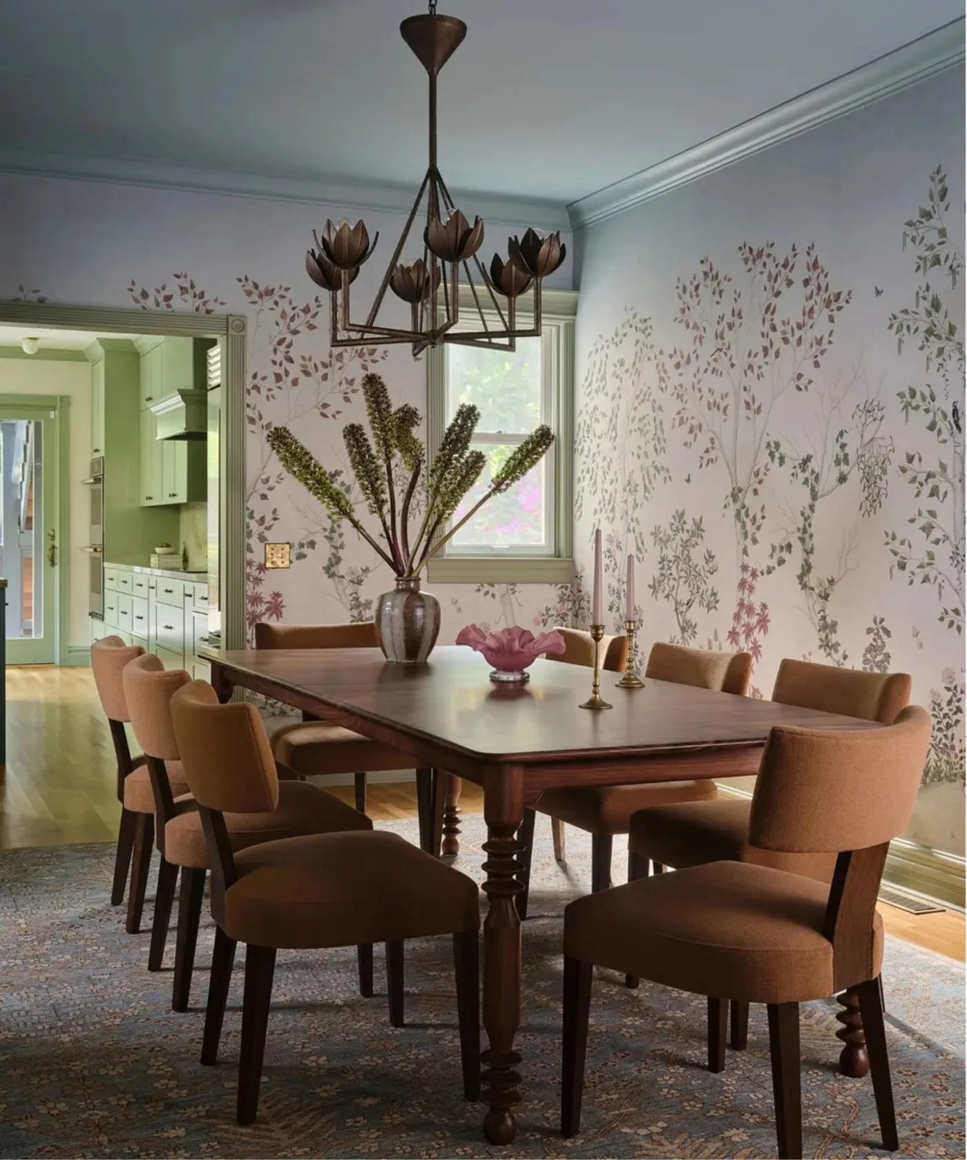 Cottage dining room with pale pink floral wallpaper, brown upholstered chairs, a dark wooden table and a flower-shaped ceiling light.
