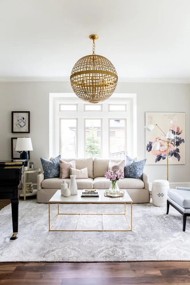 A pale sofa sits beneath a woven globe pendant beside framed art and a light rug