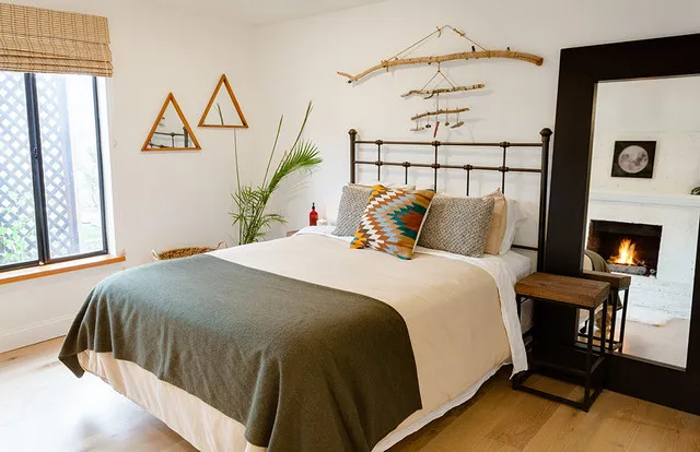 A dark metal bed sits beneath a branch-like wall decoration beside simple geometric pieces.