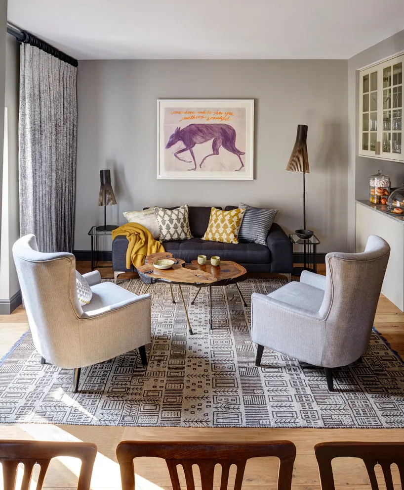 Two pale armchairs face a dark sofa beneath framed artwork