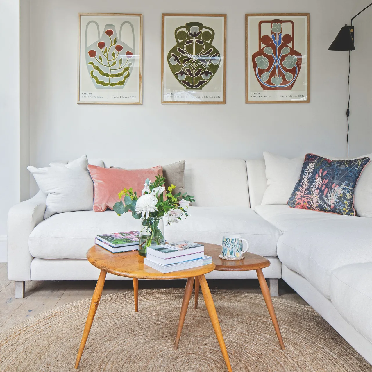 A white sectional has colorful cushions beneath three framed prints