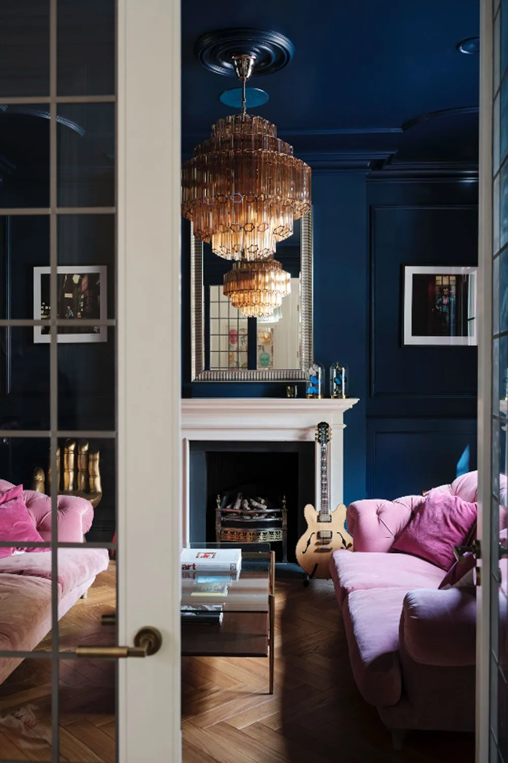Deep blue walls frame pale pink seating beside a light fireplace and warm pendant.
