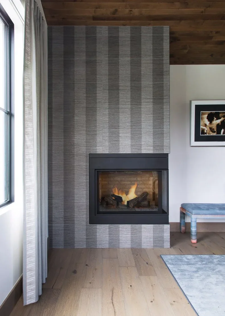 Gray striped fireplace wall with black rectangular opening, wood ceiling and blue bench