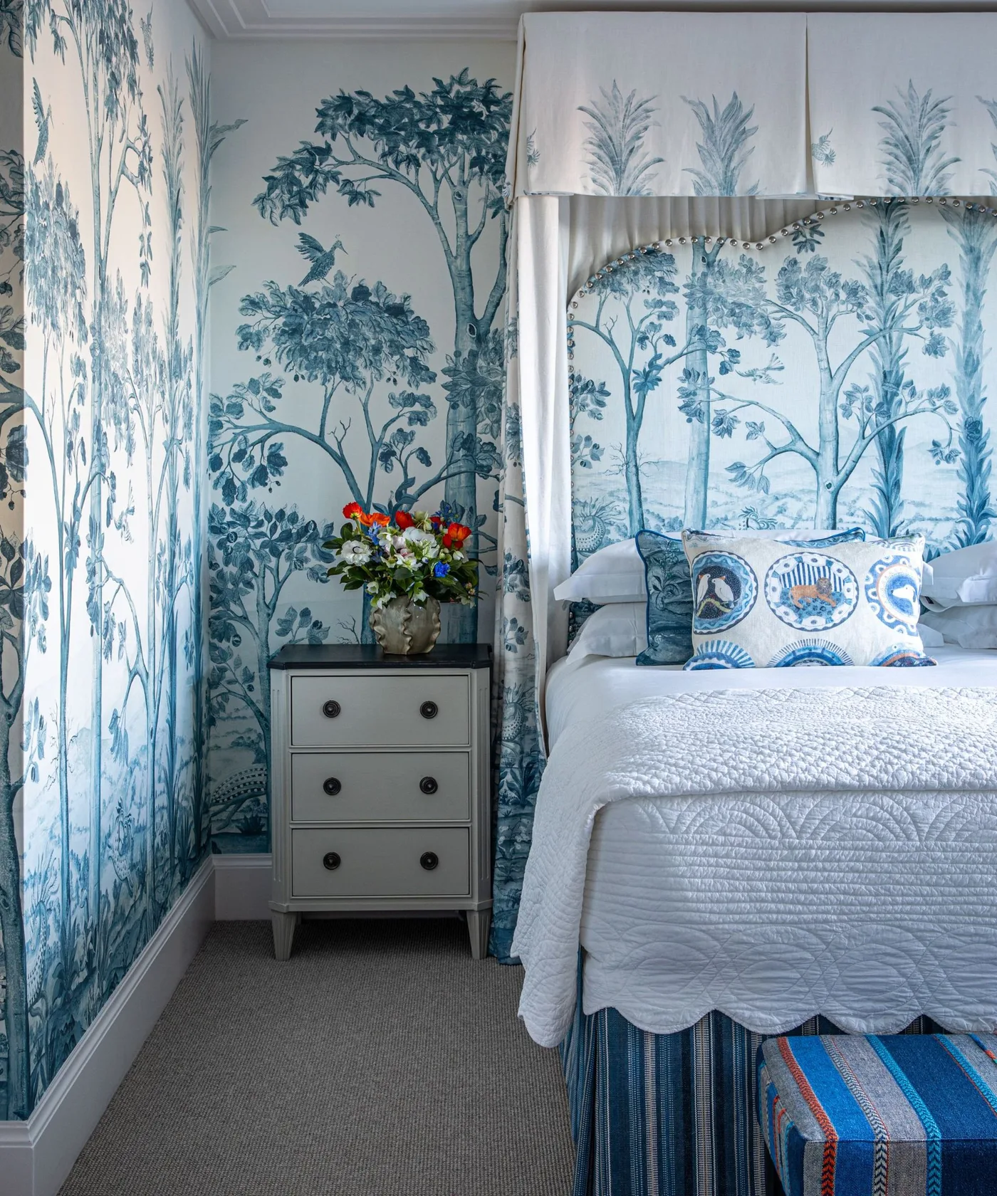Bedroom with blue tree mural wallpaper, pale canopy curtains and gray bedside drawers