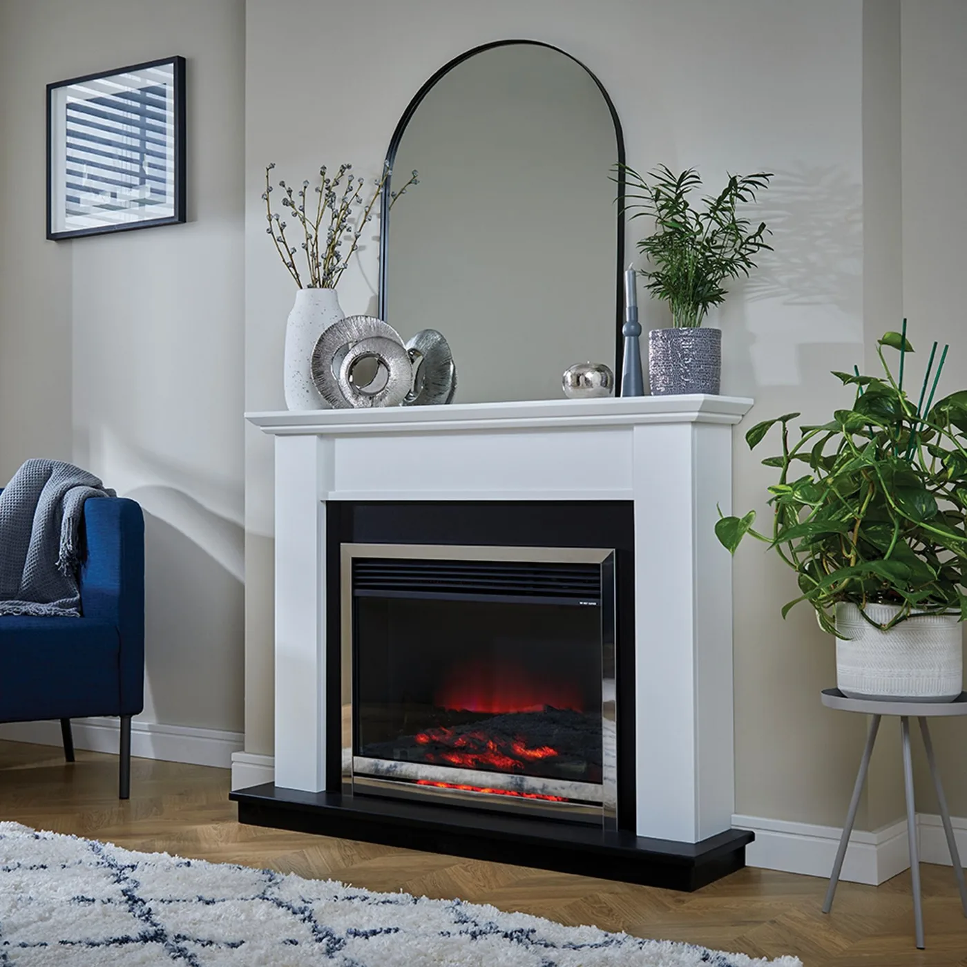 White fireplace with arched mirror, gray vessels, plant and blue chair in pale room