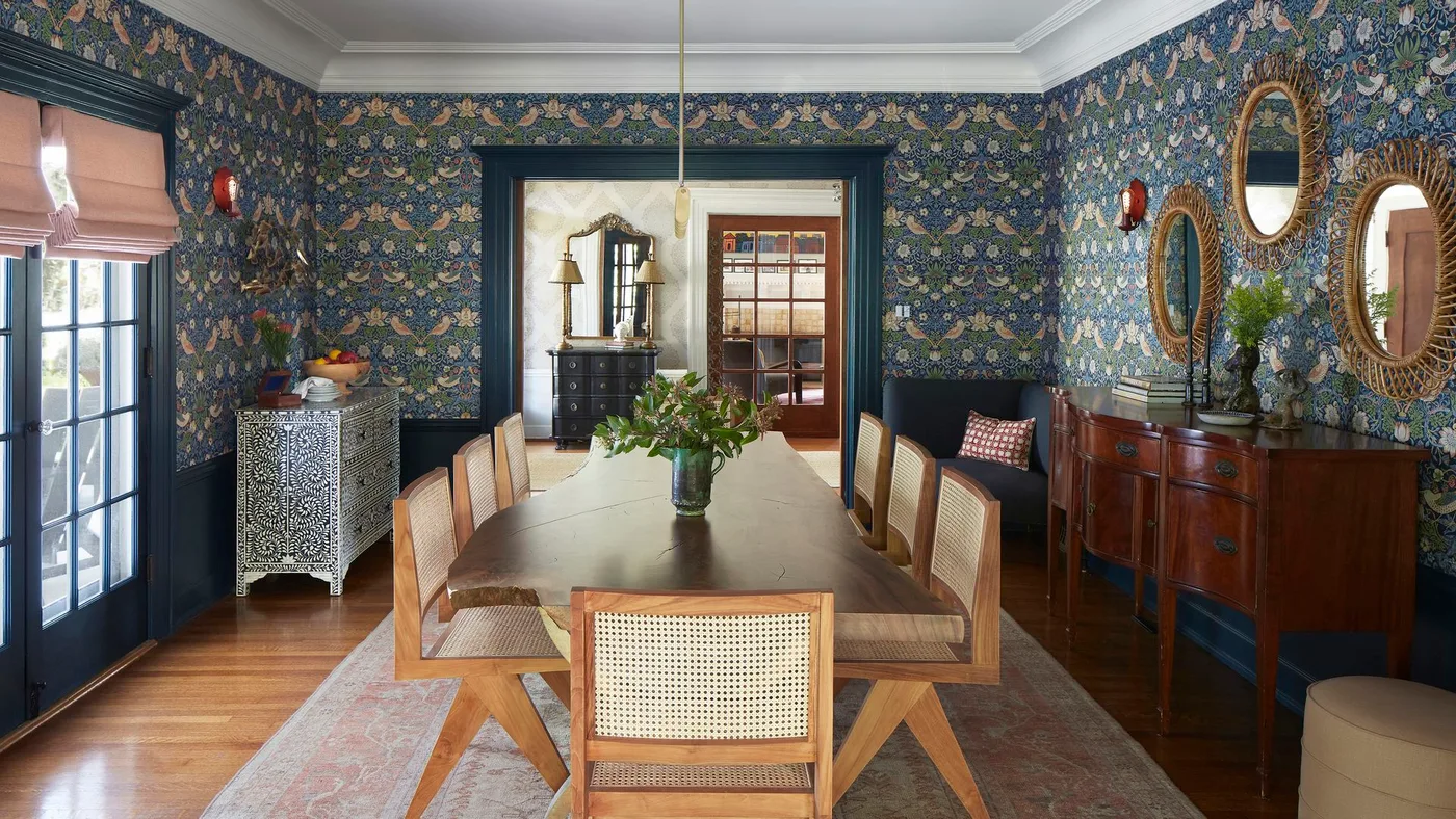 Wood dining sideboard on slim legs against blue floral wallpaper beneath three oval mirrors