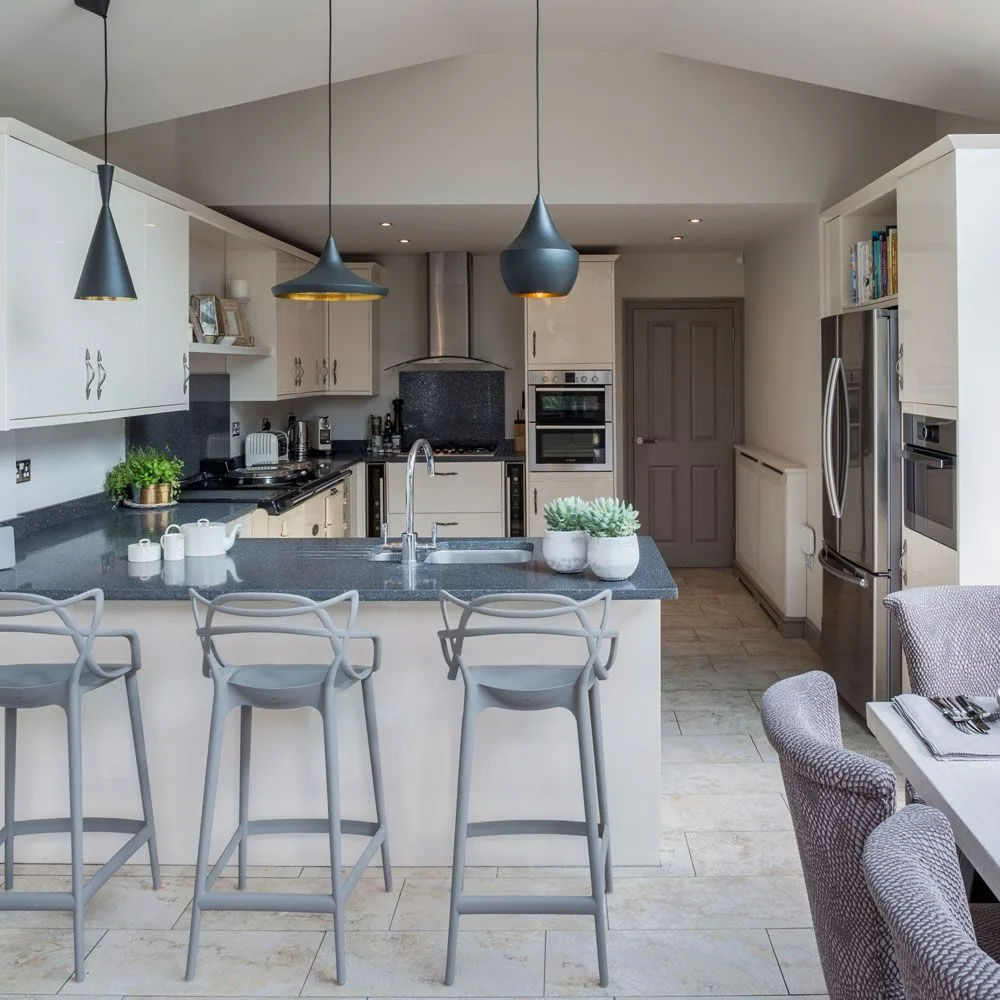 Cream kitchen cabinets and dark counters sit beneath three blue pendant lights