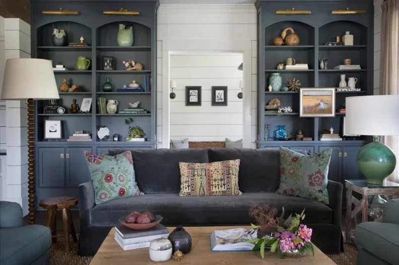 Dark sofa with patterned cushions in front of blue-gray arched bookcases, green lamps and low wood coffee table