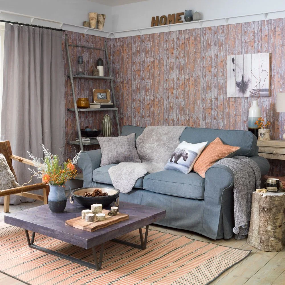 A blue sofa and wooden table sit against a wood-effect patterned wall beside a leaning ladder and plain curtains