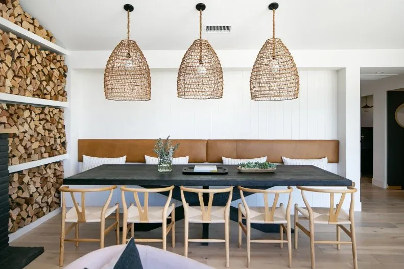 Three woven pendants in a row above a dark dining table with a brown bench and pale wood chairs