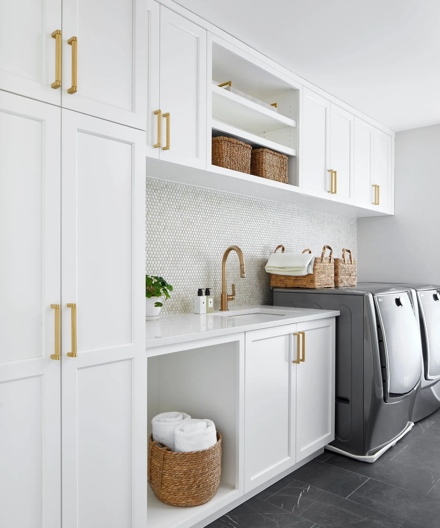 White laundry cupboards with open woven-basket shelves, pale patterned backsplash, sink and dark side-by-side appliances