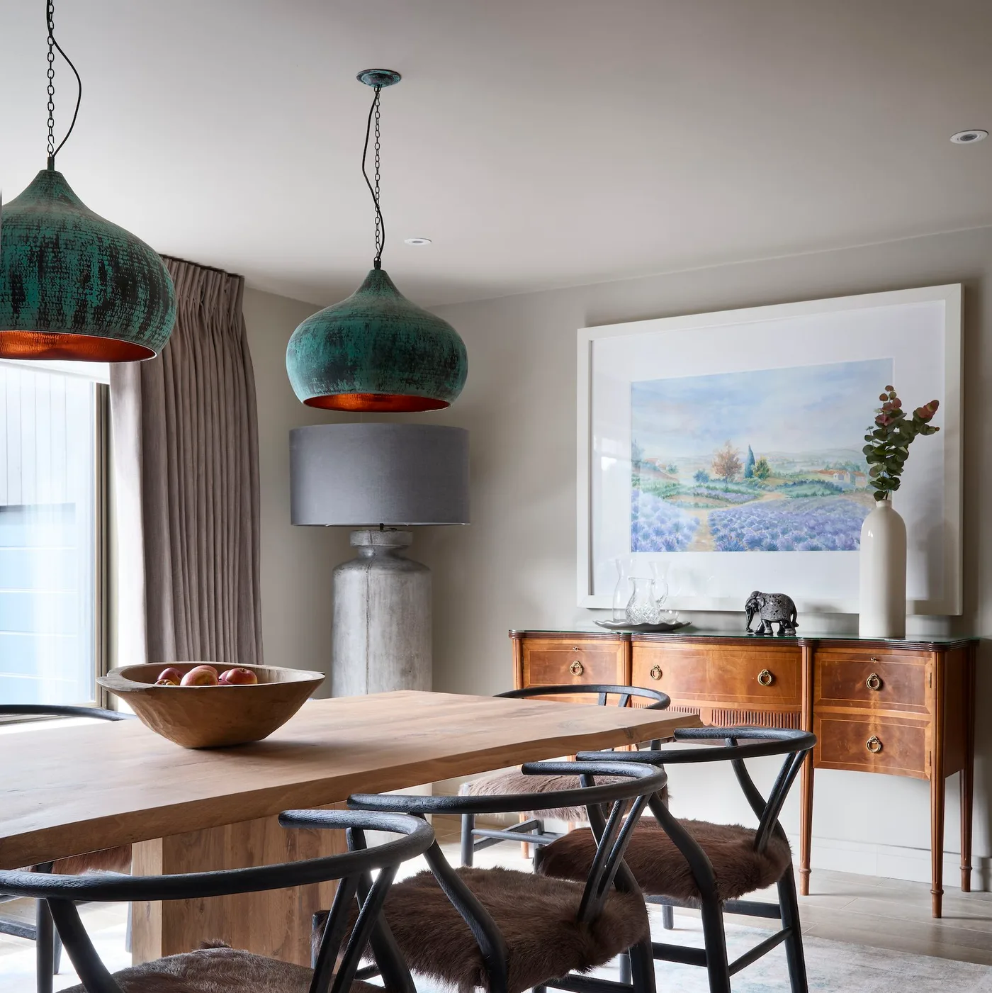 Two green-toned pendants above a wood table with a gray-shaded lamp near a wood sideboard