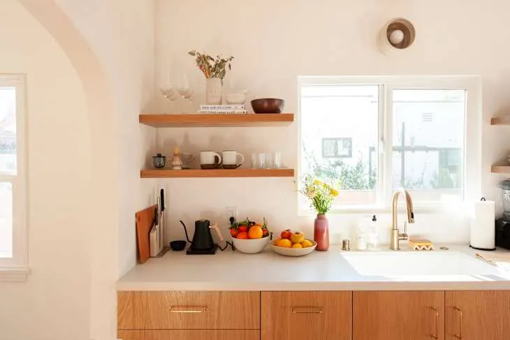 Light timber drawers beneath a kitchen window, minimal open timber shelves and ceramic fruit bowls