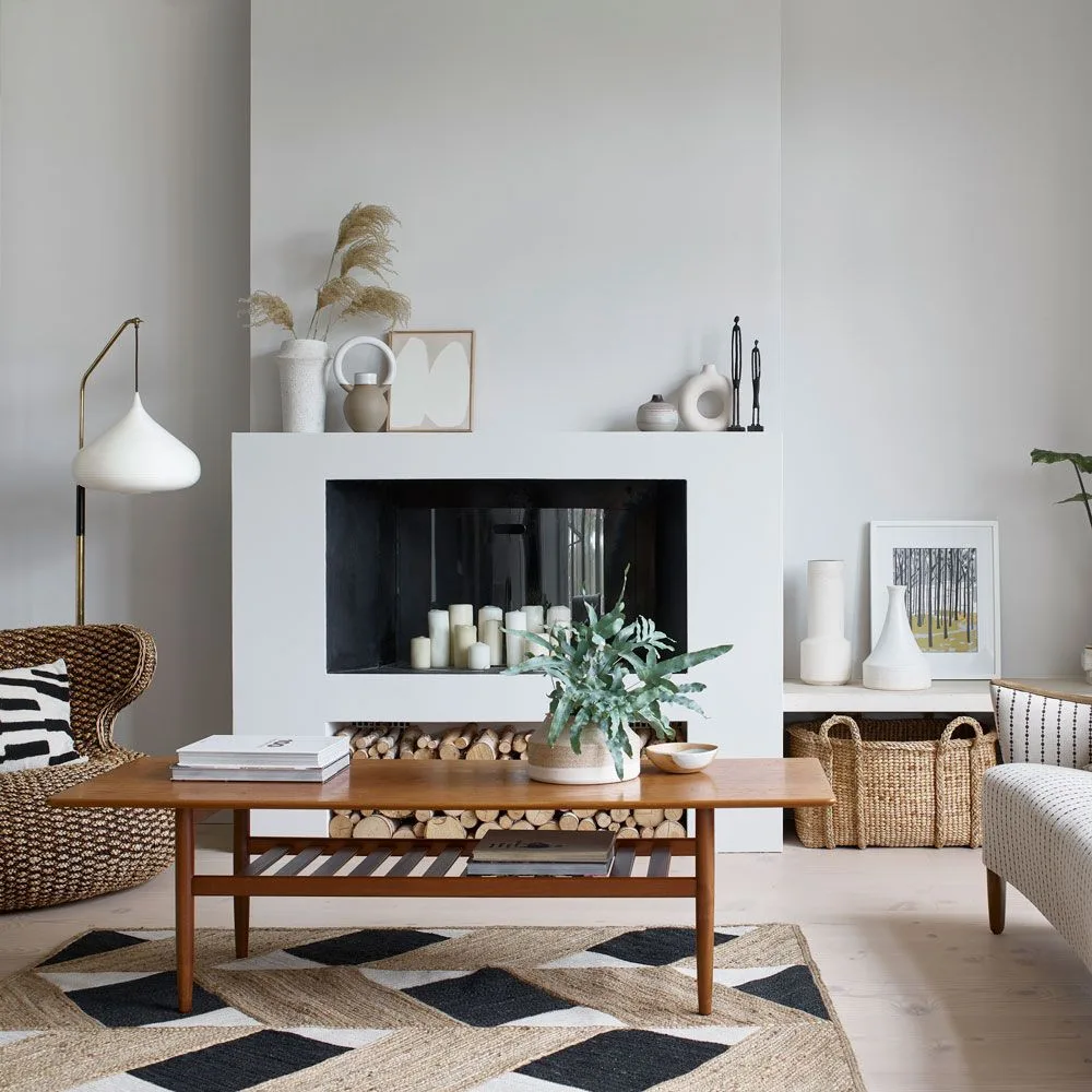 White modern mantel with pale sculptural vessels, small framed picture, slender figures and inactive candle-filled opening