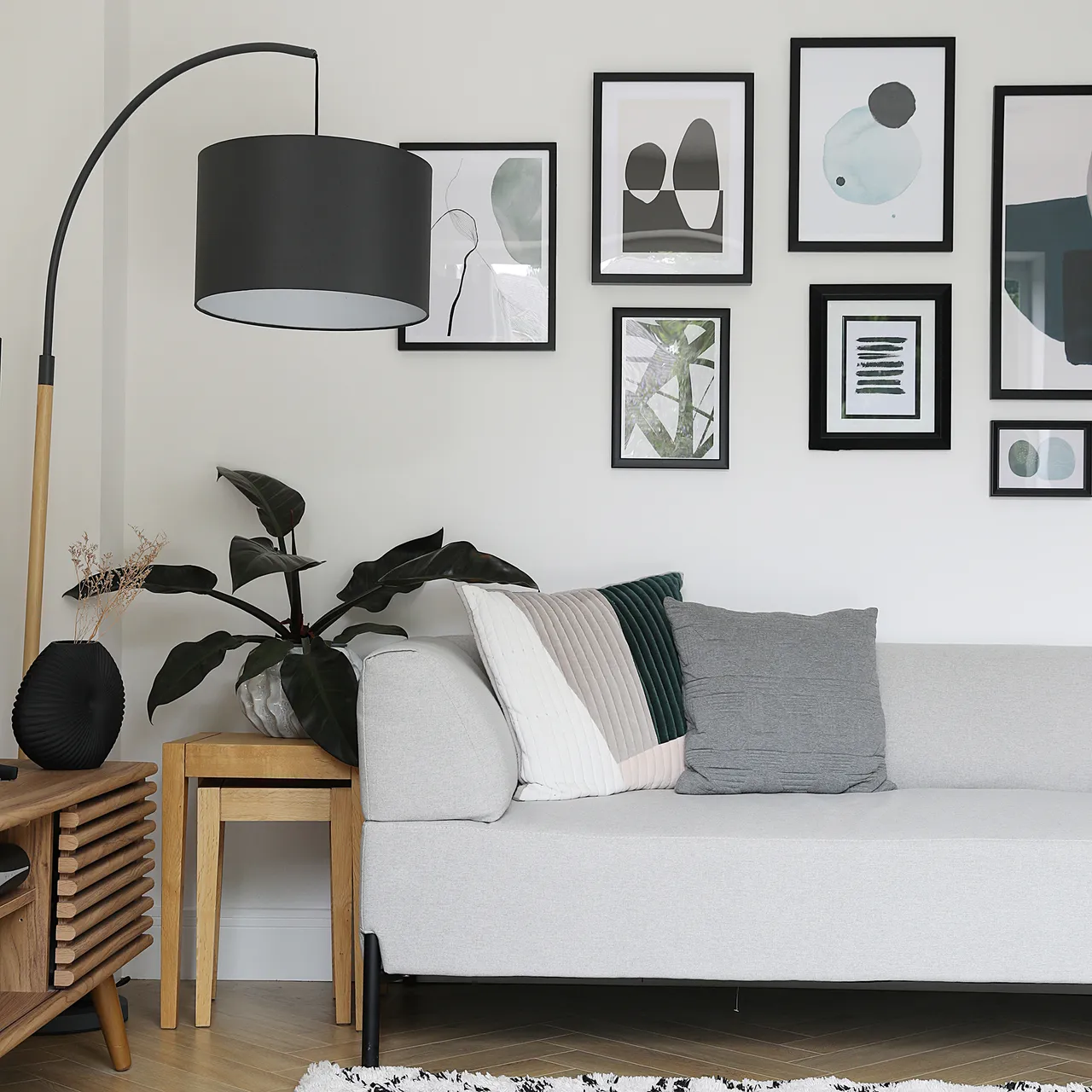 A light sofa sits beneath black-framed artwork beside a curved floor lamp