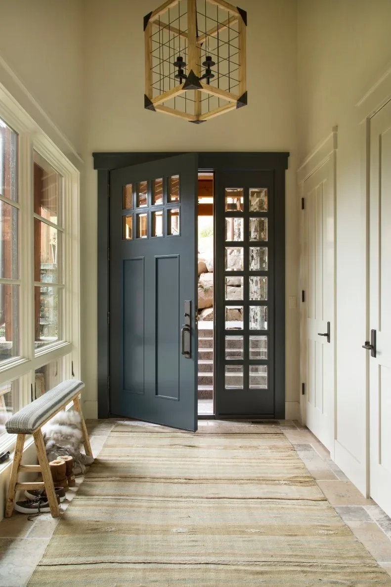 Gold-colored cube candle lantern with wire grid above pale country hall, gray glazed front door, narrow bench and long striped rug