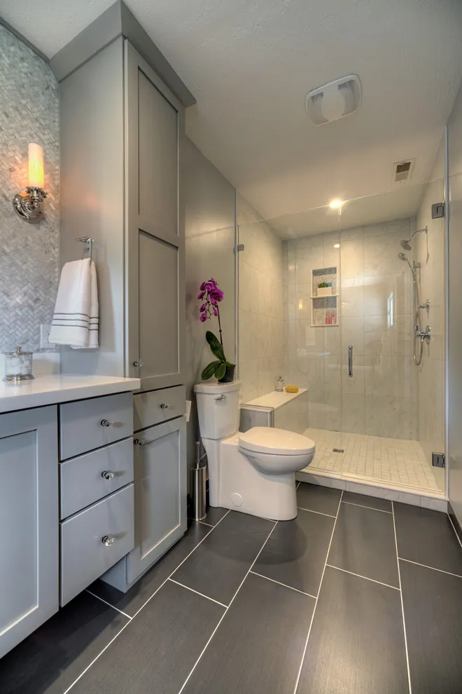 Large gray rectangular tiles cover a long bathroom floor below gray cabinetry