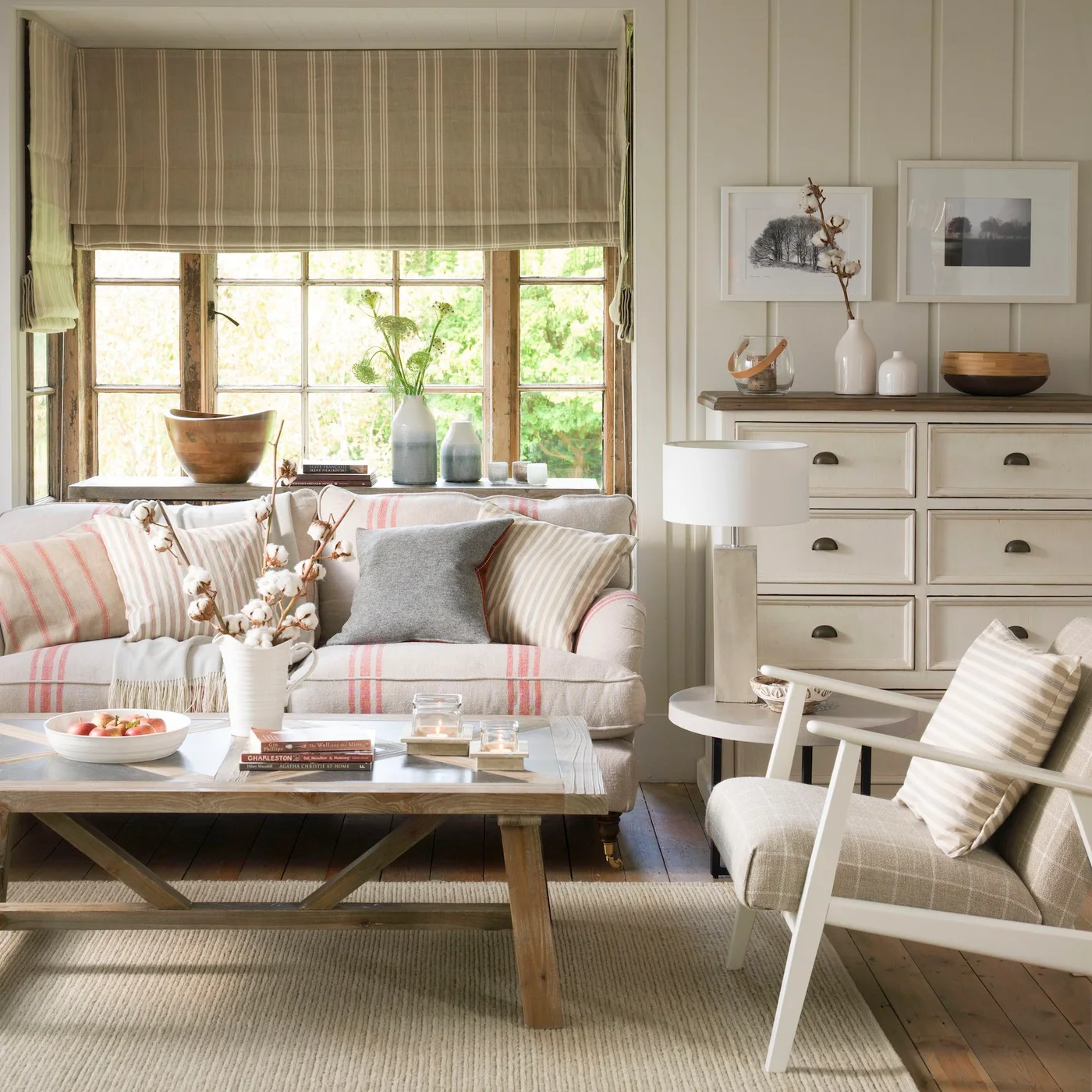 A pale striped sofa sits beside a wooden coffee table, a painted drawer unit and a light wooden chair