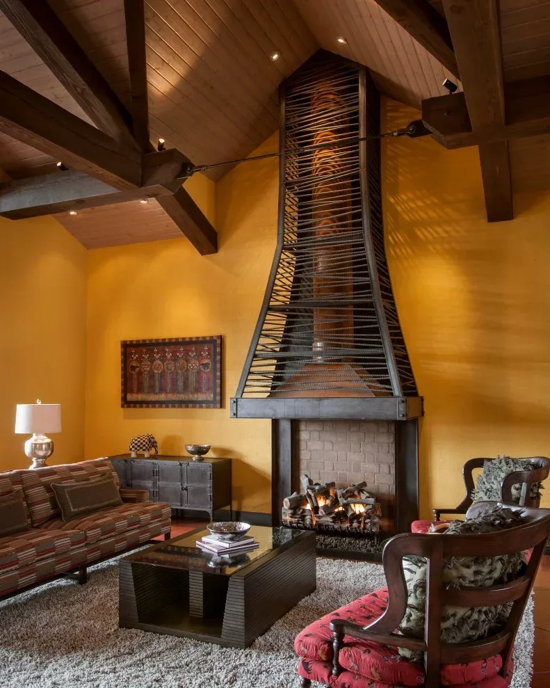 Yellow fireplace wall behind tall metal hood and pale brick opening beneath wood pitched ceiling