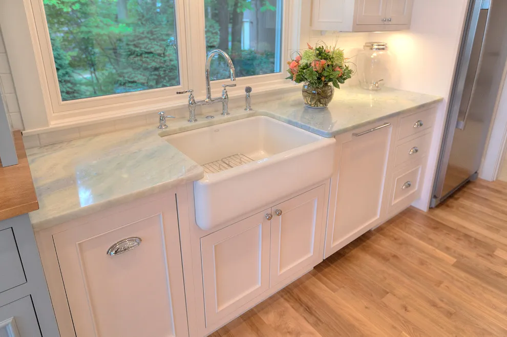 Pale cream-pink cabinet fronts sit beneath a white apron sink and white-framed windows