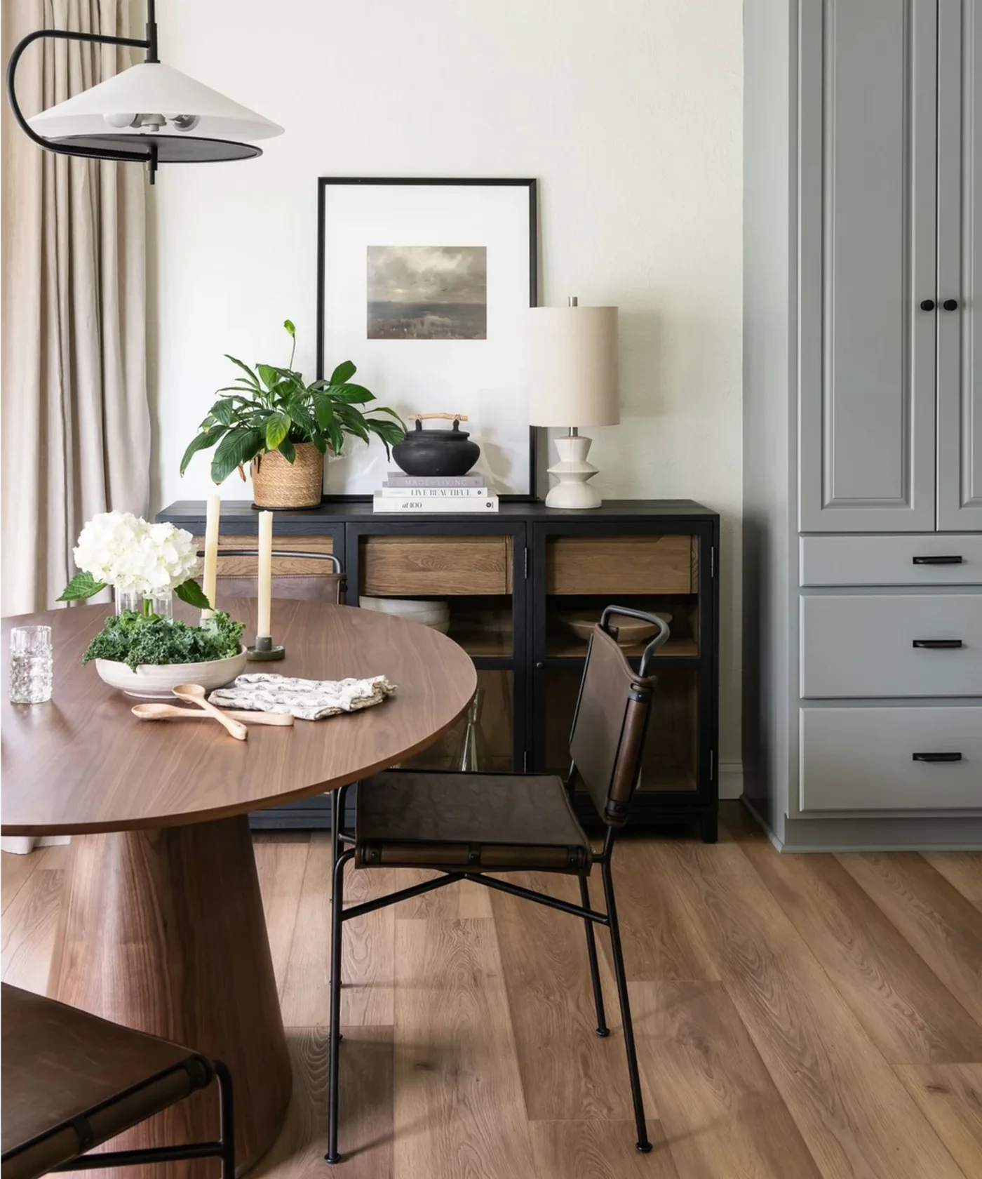 Black glazed dining cabinet with woven baskets inside beside a brown table and a tall gray cupboard