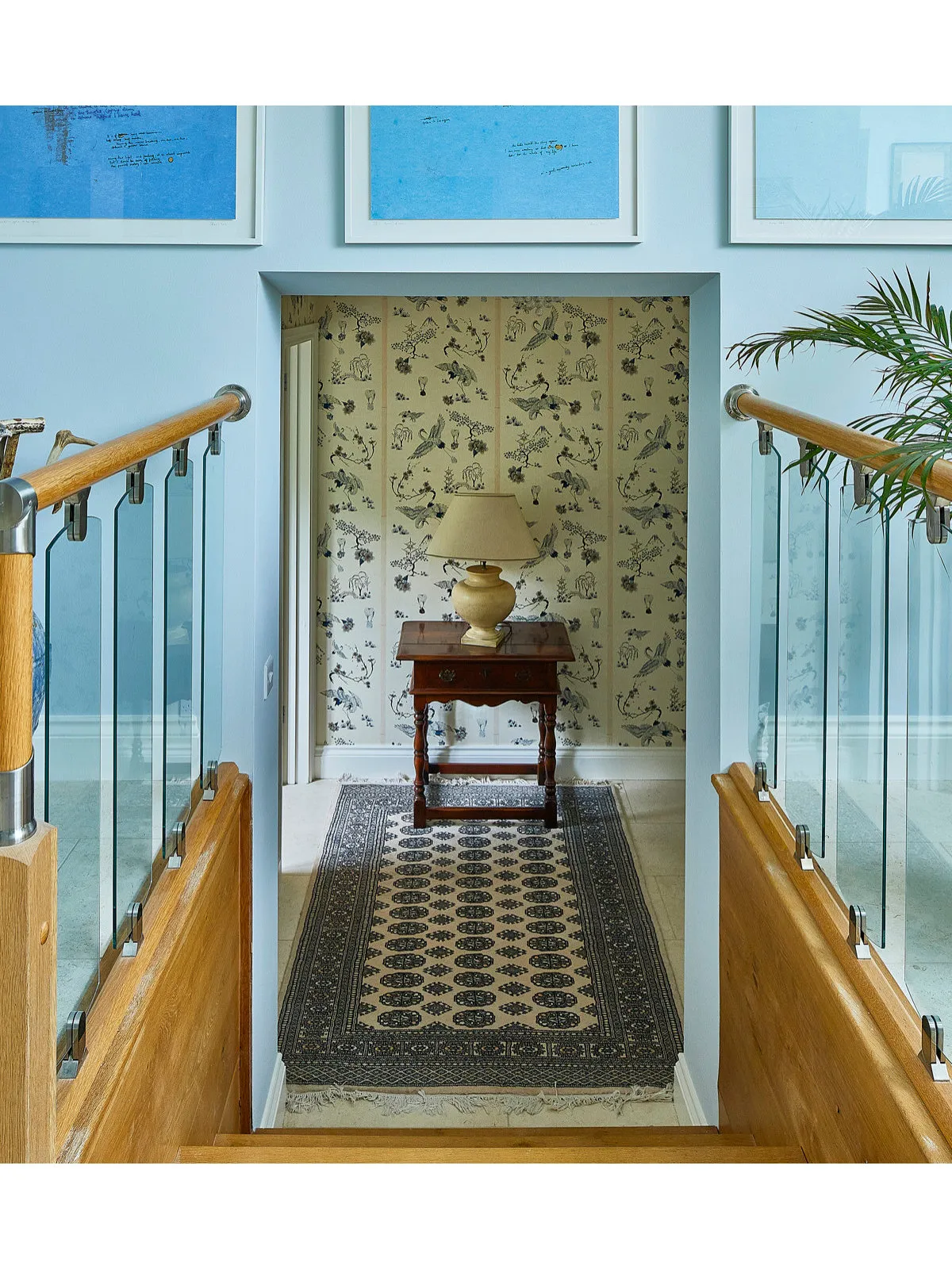 A dark patterned runner leads through a hallway with pale blue walls, timber rails and framed pictures.