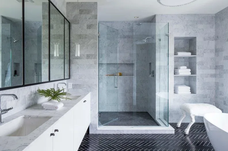 Bathroom with a charcoal herringbone floor and pale grout, white vanity and tub, light gray walls, glass shower, and open towel niches.