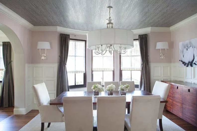 Dining room with pale pink upper walls, white paneling, a broad white drum chandelier, pale chairs and a dark wood table