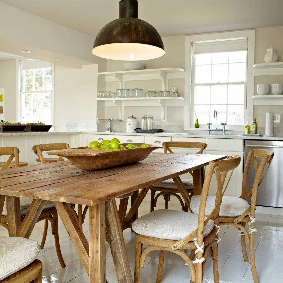 White bracketed shelves with glasses and bowls around a kitchen window behind a wood dining table