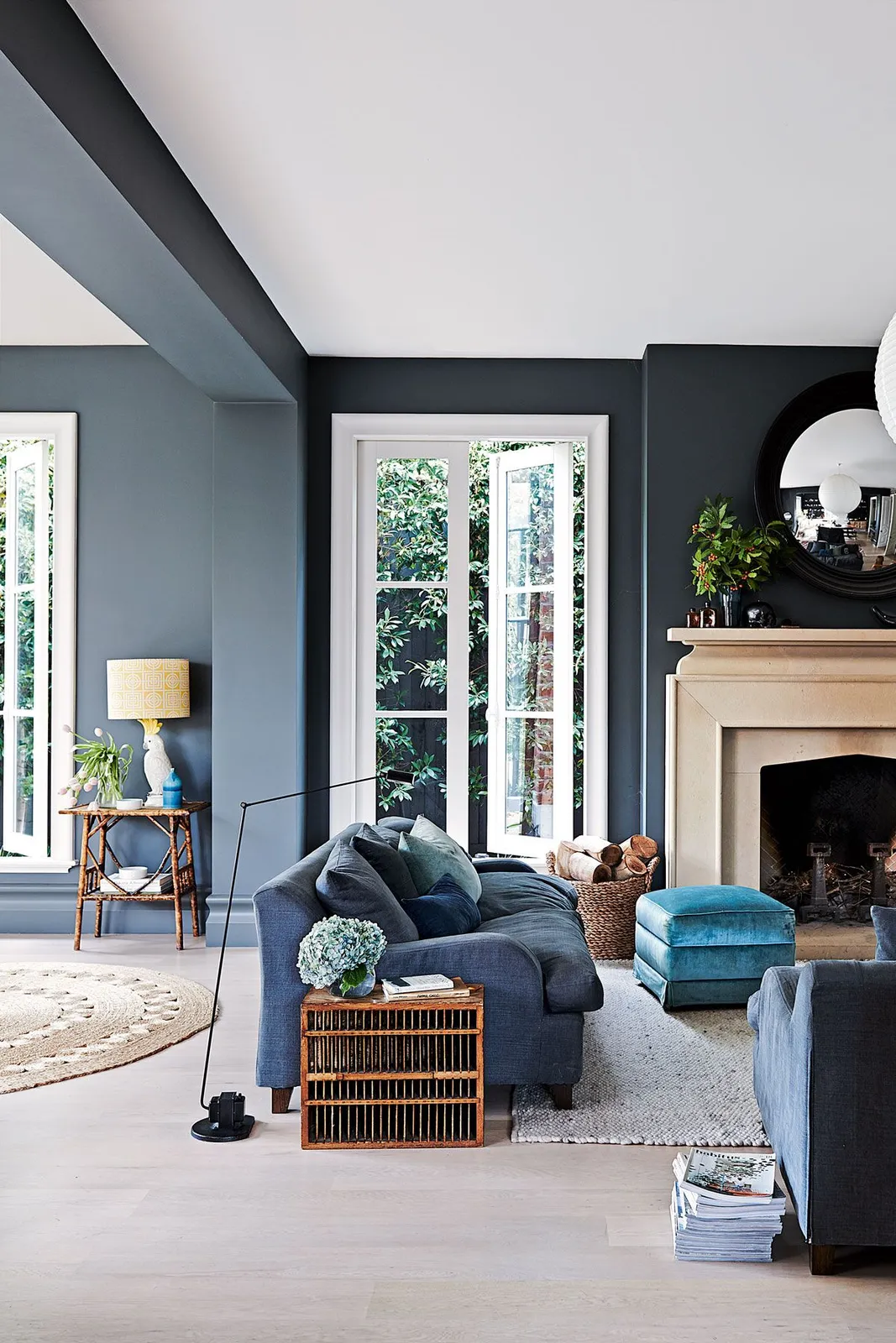 Deep blue-gray walls and a beam meet a pale ceiling above blue seating, a turquoise ottoman and a light rug.