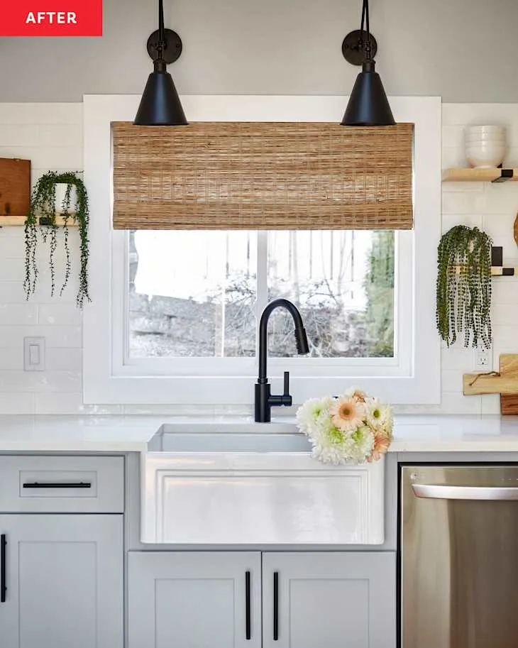 White apron-front sink framed by plants, woven roman shade and black task lights