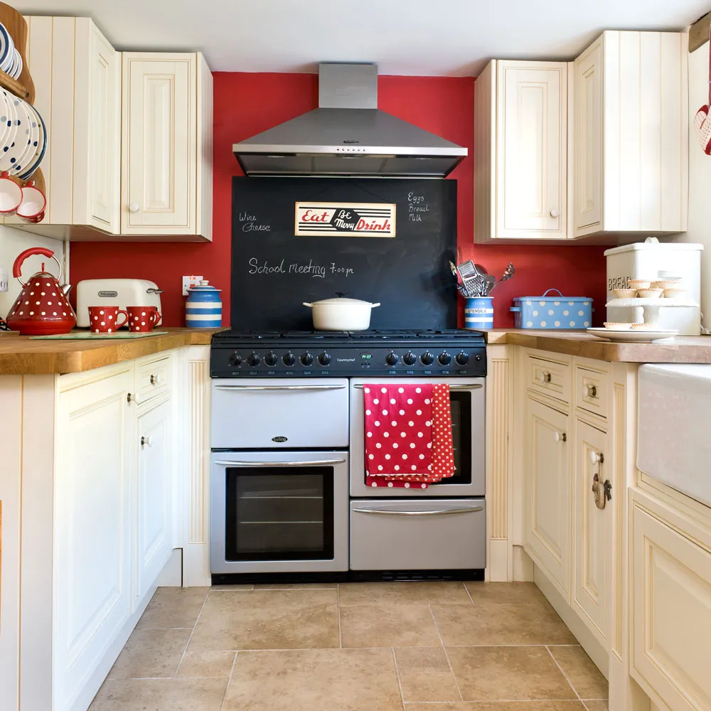 Cream cabinets frame a red wall and a black backsplash behind a range cooker