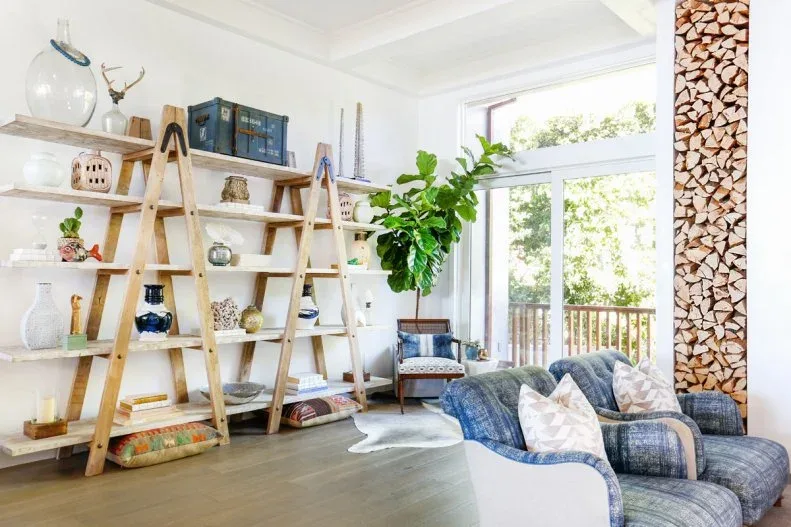 White living room with ladder-style open shelving, a blue chair and tall leafy plant beside glazed doors.